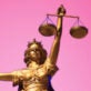 A close-up of the statue of justice holding scales against a pink background.