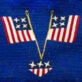 Two American flag ribbons embroidered on a bold blue canvas, forming an inverted 'v' shape with a star-studded tail descending from the intersection.